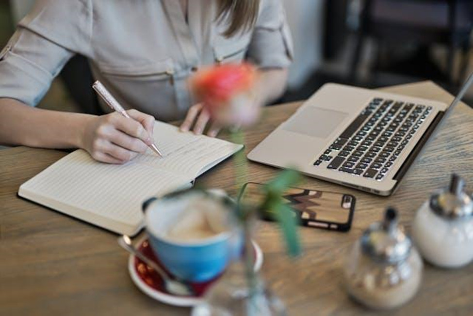 A person writing on a notebook beside a Macbook